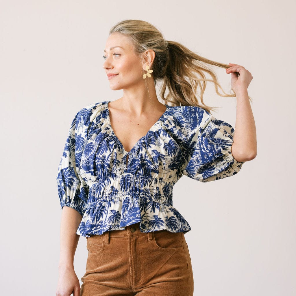 Woman wearing a blue and white floral blouse with brown pants against a plain background