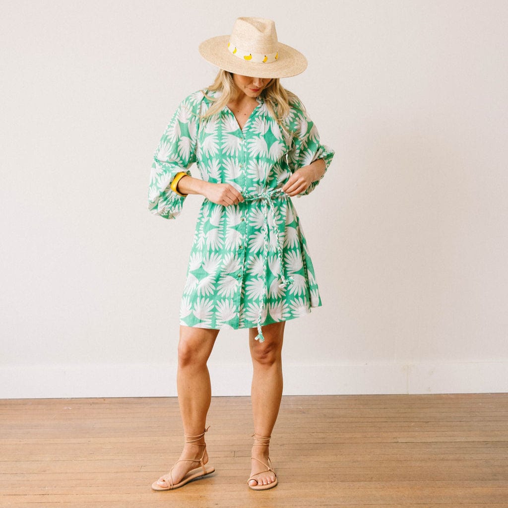 Woman wearing a green and white patterned dress with a hat on a plain background