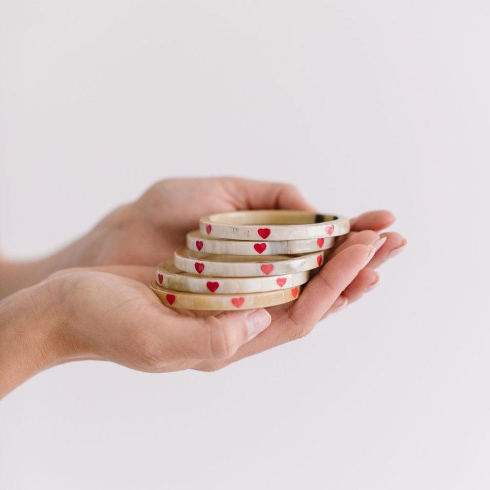 A hand holding a stack of bangles with red heart patterns on them, against a white background.